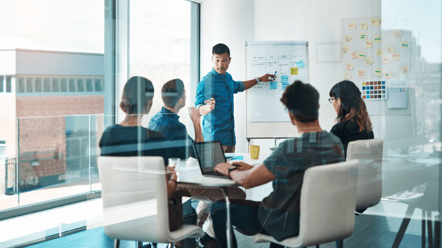 Team bei einer Präsentation – Ein Mitarbeiter erklärt eine Strategie auf einem Flipchart.